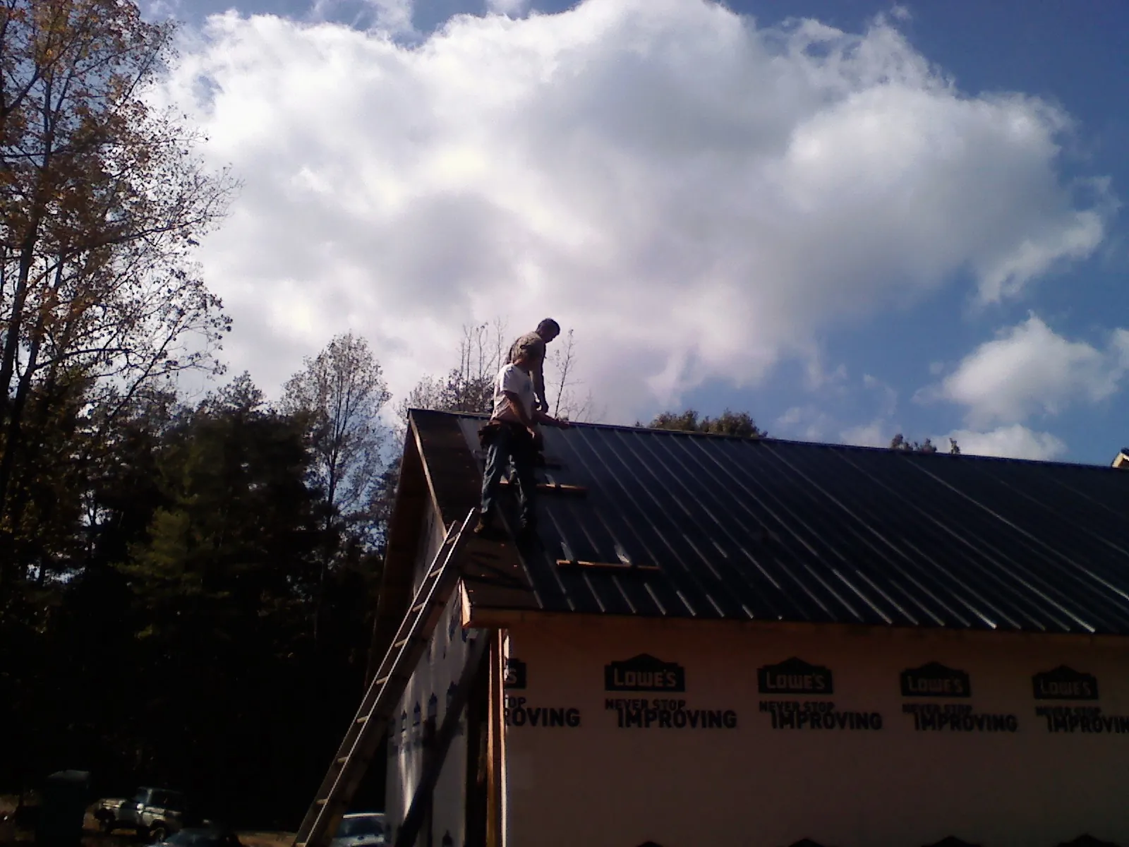Roofer fastening dark metal panels high against a cloudy sky, from a Roof Inspection job in Goshen